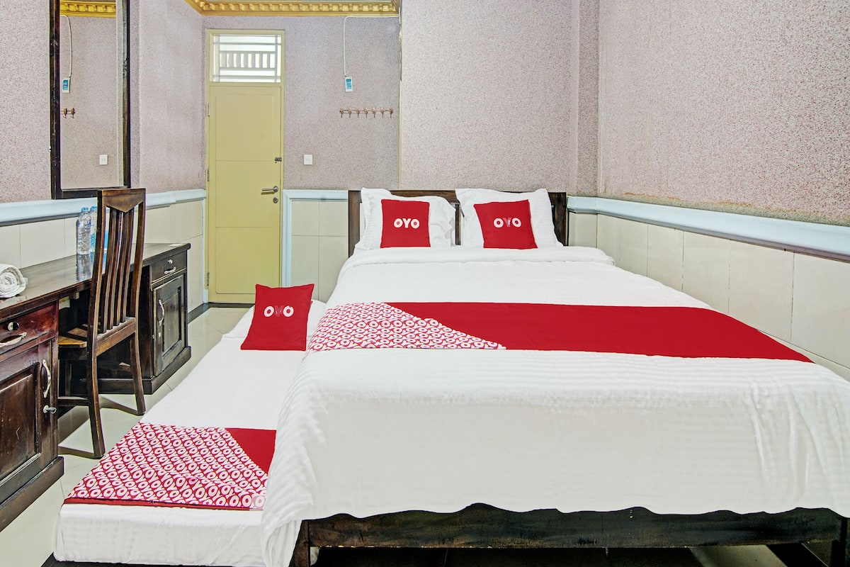 A hotel room with two beds, a wooden desk, a mirror, and a door.