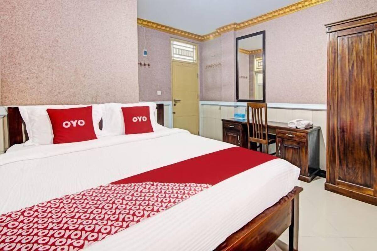 A hotel room with a bed, a wooden wardrobe, a desk, and a mirror.