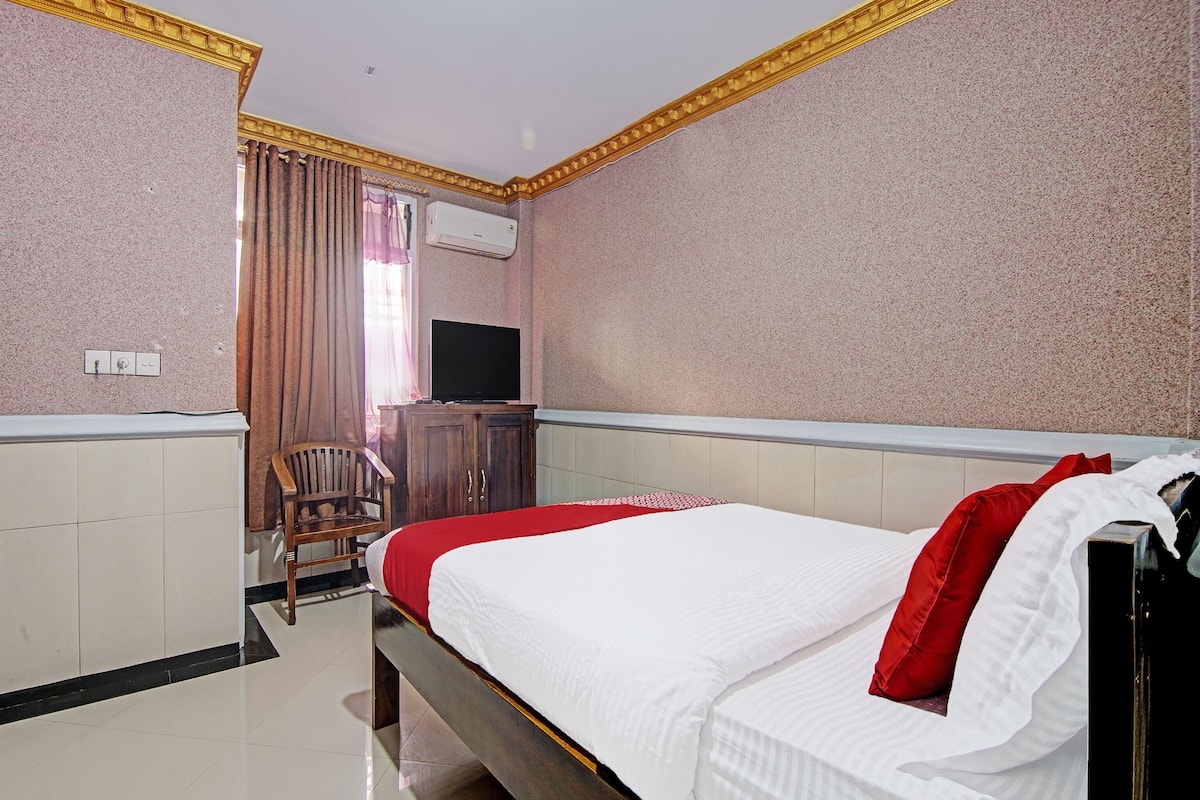 A hotel room with a bed, a television, a wooden chair, and a wardrobe.