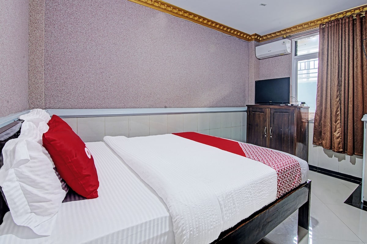 A hotel room with a bed, a television, a wardrobe, and a window with curtains.