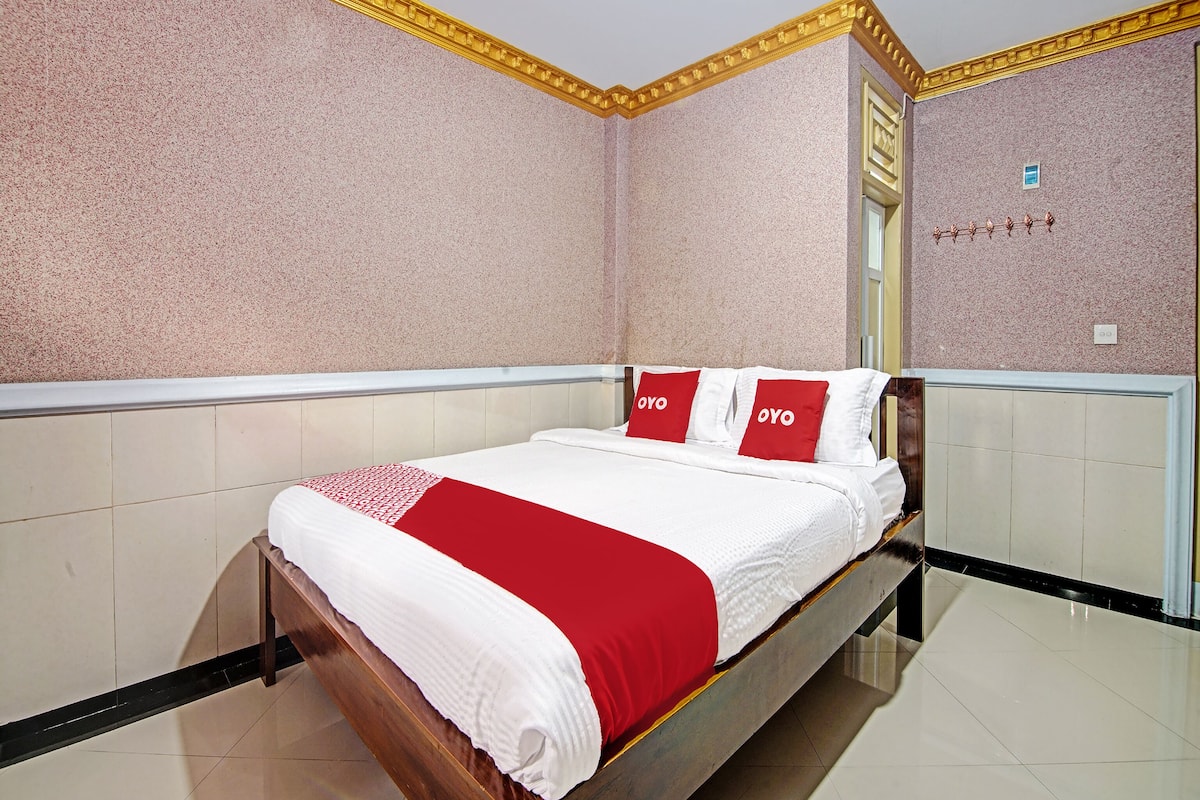 A hotel room with a bed, a red and white bedspread, and a wall with a textured pattern.
