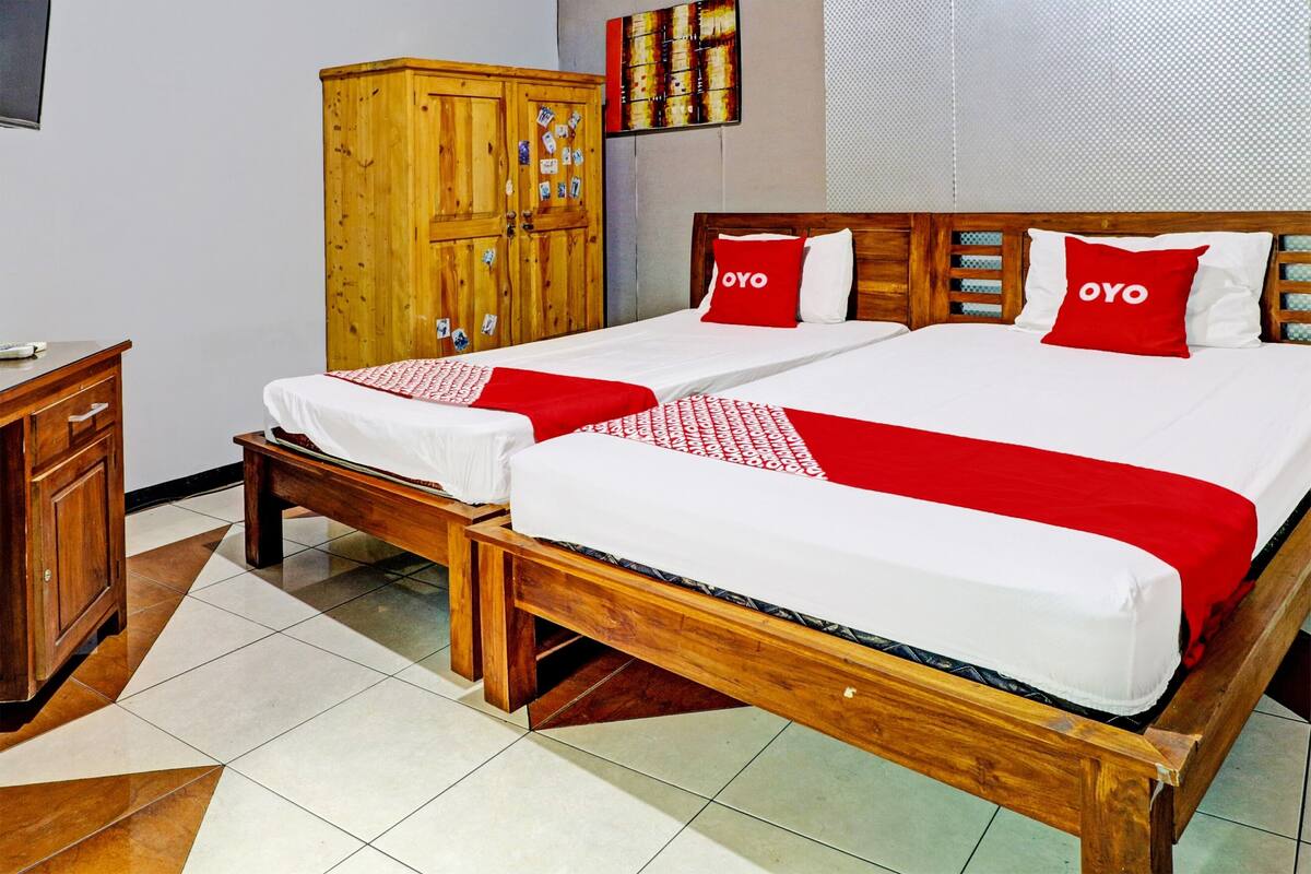 A double bed with two red pillows, a wooden wardrobe, and a tiled floor.