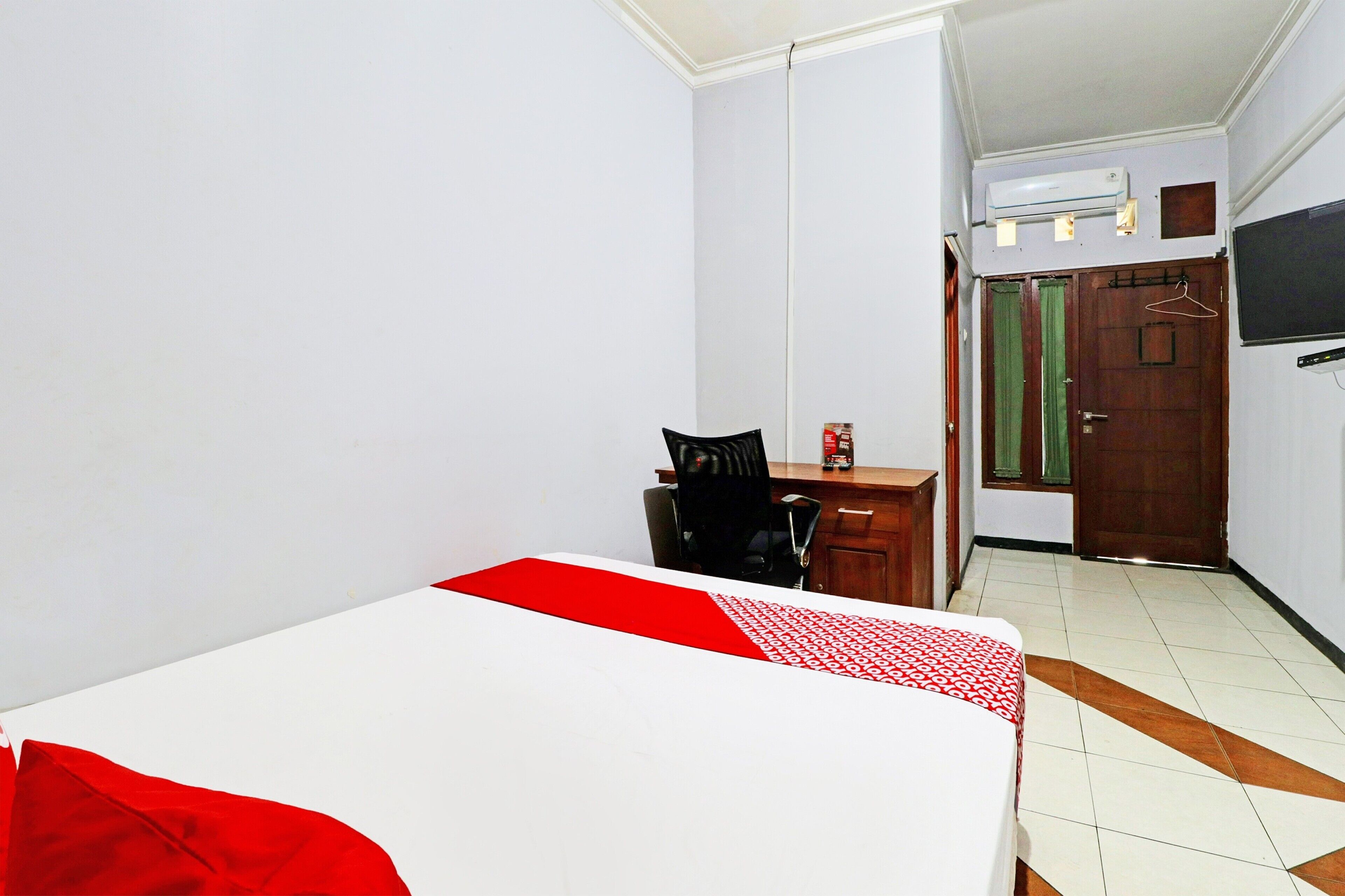 A hotel room with a bed, a desk, a chair, and a TV mounted on the wall.