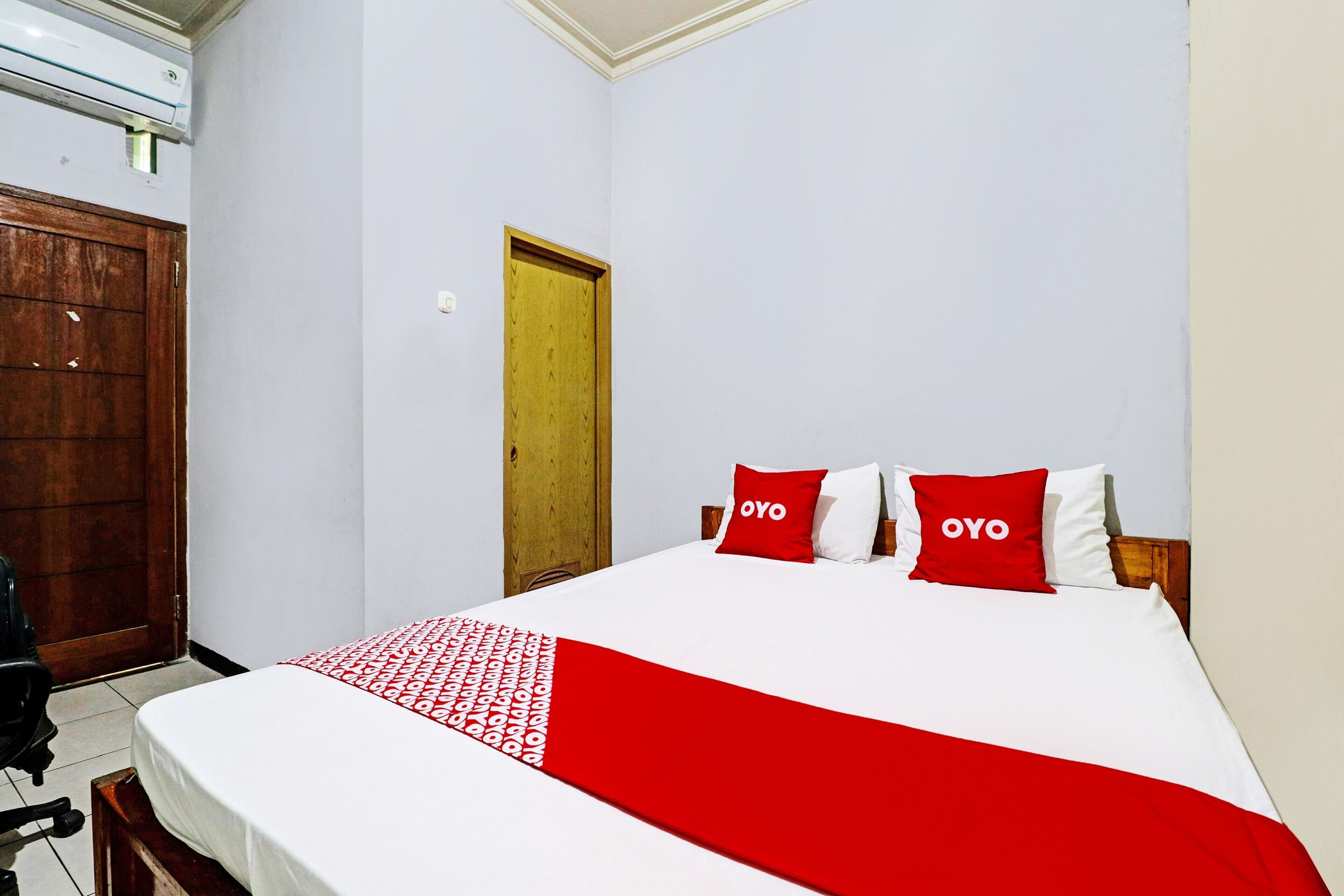 Une chambre à coucher avec un lit, deux oreillers portant le mot « OYO », une porte en bois et un appareil de climatisation.