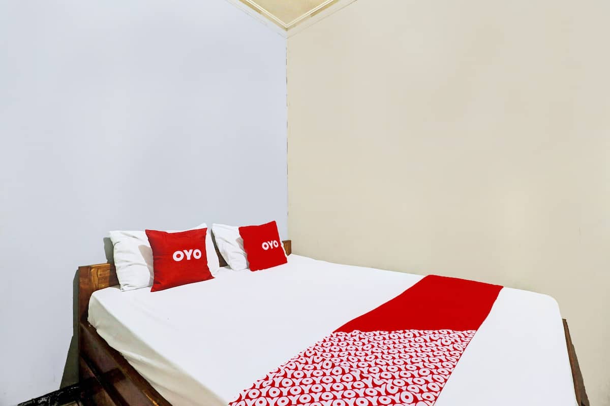 A bed with a white and red bedspread, two red pillows with the word "OYO" on them, and a wooden headboard.