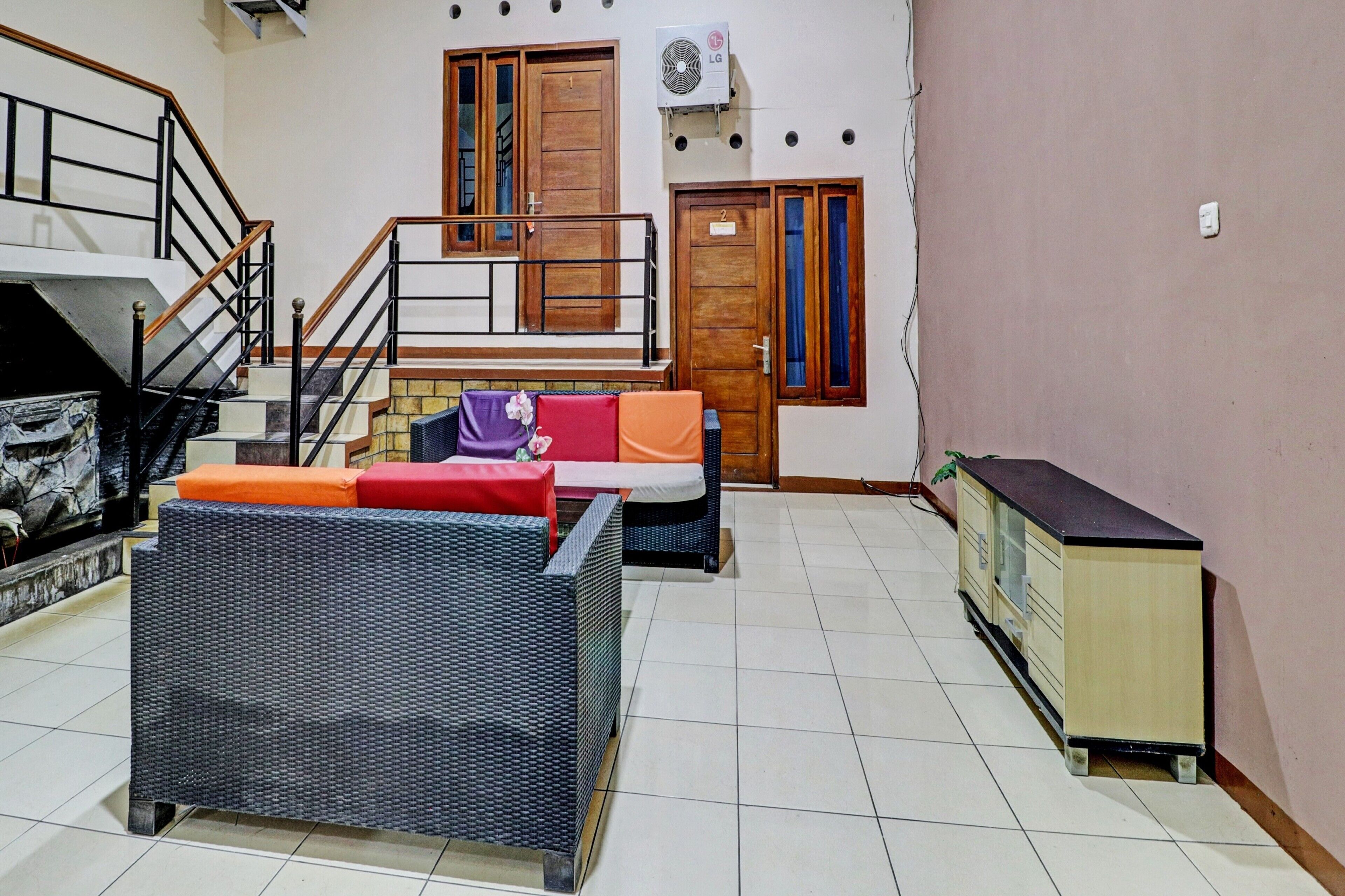 A living room with wicker furniture, a staircase, and a kitchenette.