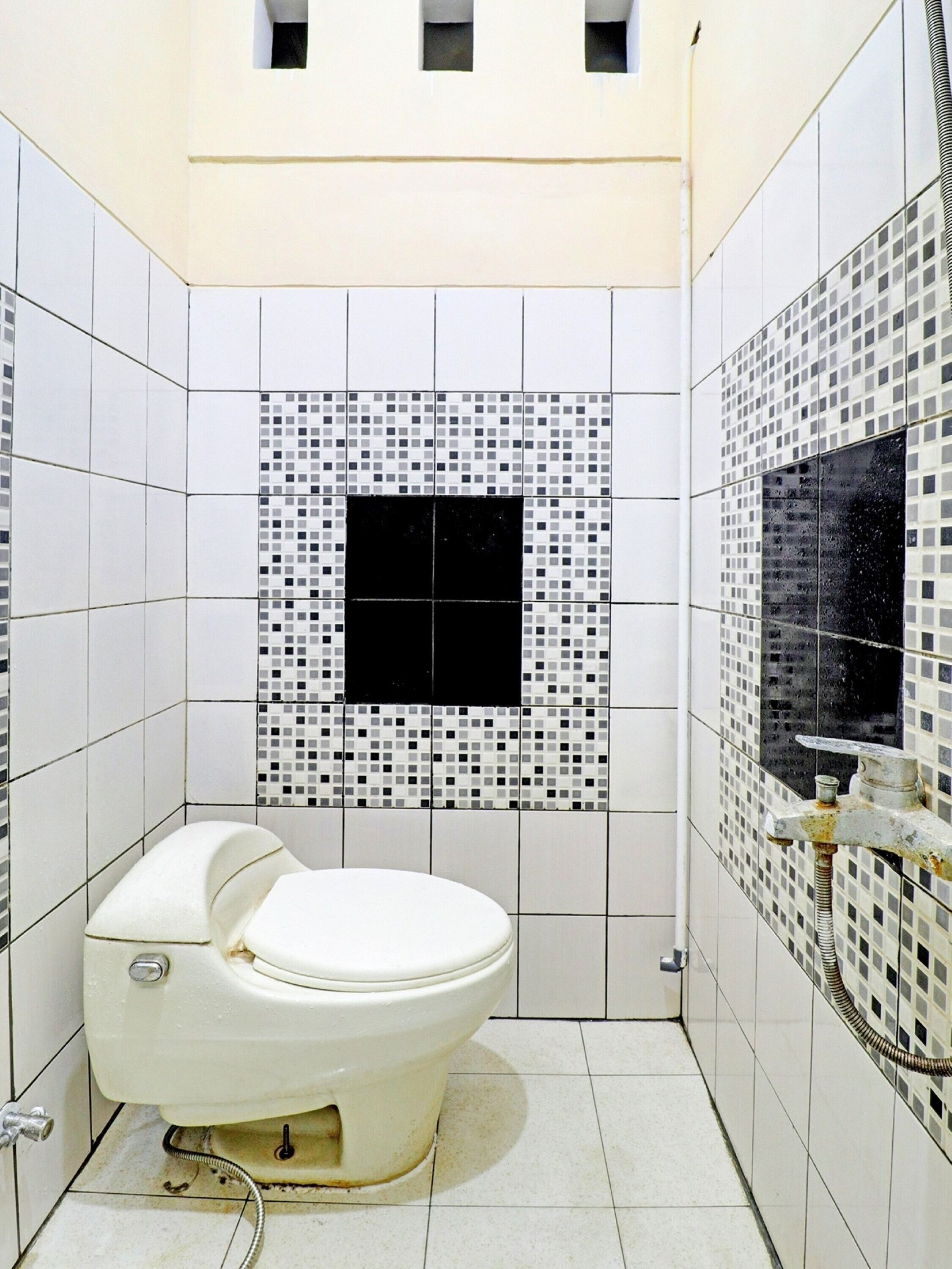 A bathroom with a white toilet, tiled walls, and a black square tile in the center.
