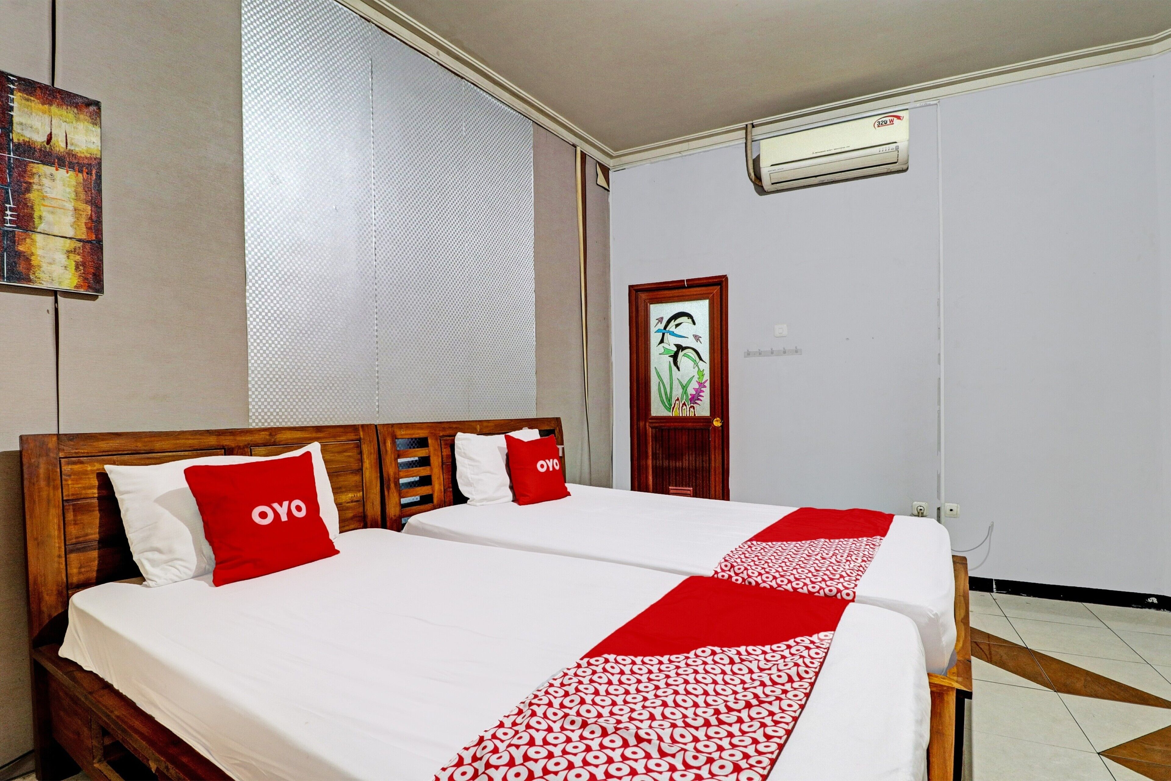 A hotel room with two beds, a wooden headboard, a red and white patterned bedspread, and a window with blinds.