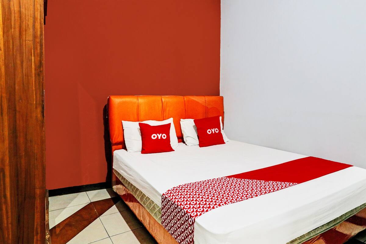 A neatly made bed with a red and white patterned bedspread and two red pillows with the word "OYO" on them.
