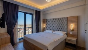Een moderne slaapkamer met een groot bed, een houten nachtkastje, een aan de muur bevestigde televisie en uitzicht op de stad door een groot raam.