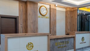Een receptiegedeelte met houten lambrisering, een klok en receptiebalies met de aanduidingen 'Topcu Grup' en 'Regulus Thermal Spa'.