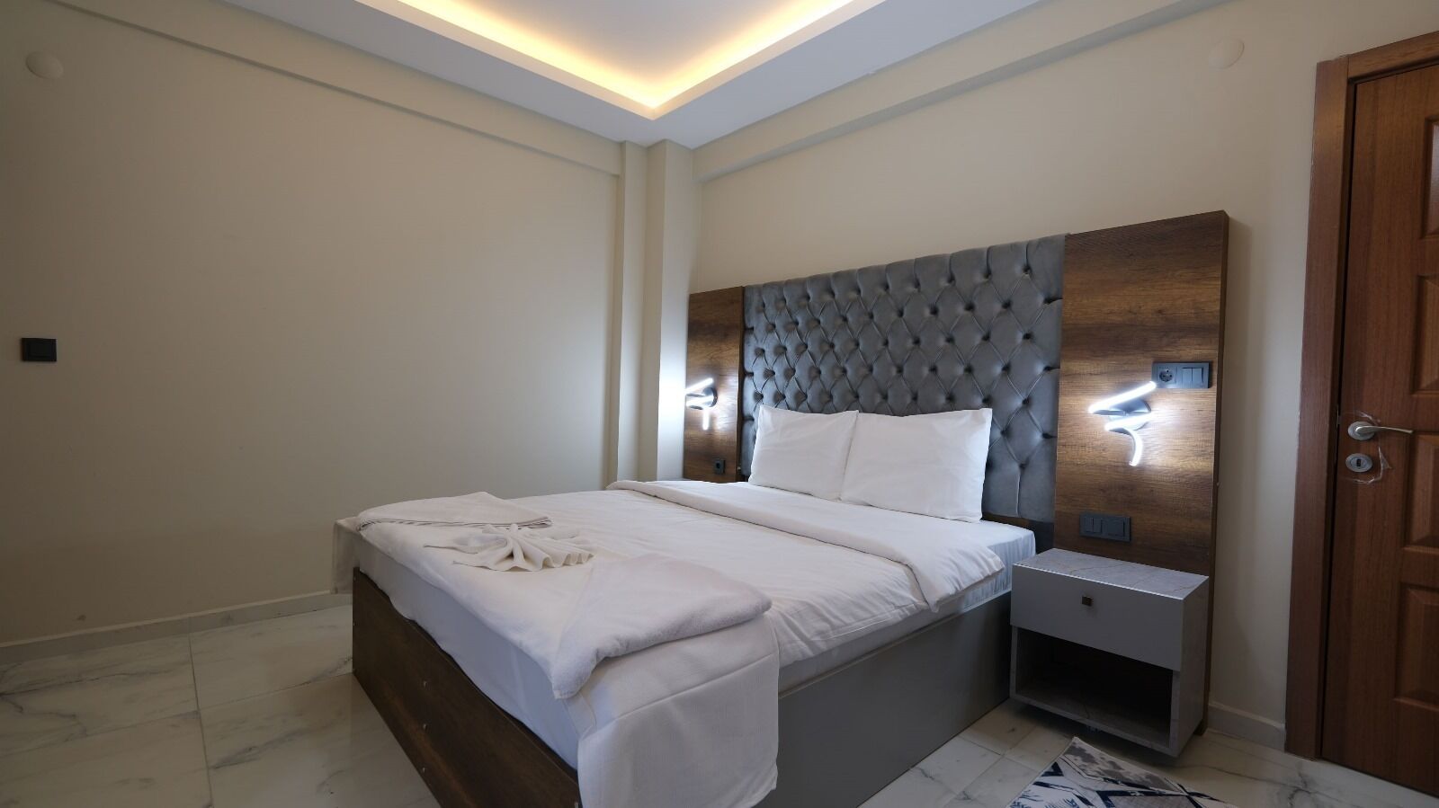 Un dormitorio moderno con una tapizada, una mesita de noche con lámpara y una cama bien tendida con sábanas blancas.
