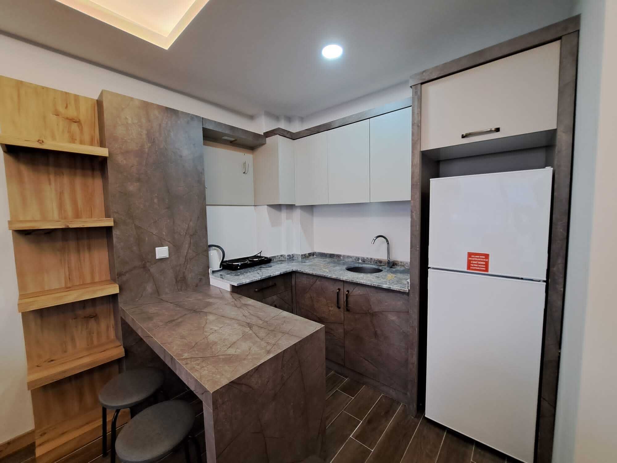 Una cocina compacta con isla integrada, estantes de madera y un refrigerador.