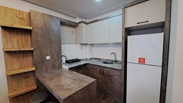 Una cocina compacta con isla integrada, estantes de madera y un refrigerador.