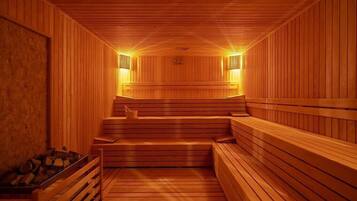 A sauna with wooden benches and walls, a bench in the center, and a firebox with logs on the left.