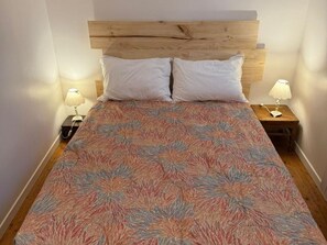 A bed with a wooden headboard, two white pillows, a floral-patterned bedspread, and two bedside lamps on wooden nightstands. - Terraced house in Barfleur with private courtyard - Pets allowed (Barfleur)