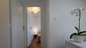 A narrow hallway with wooden flooring, a white door on the left, and a white dresser with a potted orchid on the right. - Terraced house in Barfleur with private courtyard - Pets allowed (Barfleur)