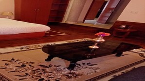 Un dormitorio con cama, mesita de noche, una mesa con un florero y una alfombra estampada con motivos florales.