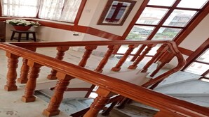 Una escalera de madera con barandilla, una planta en maceta y una cruz en la pared.