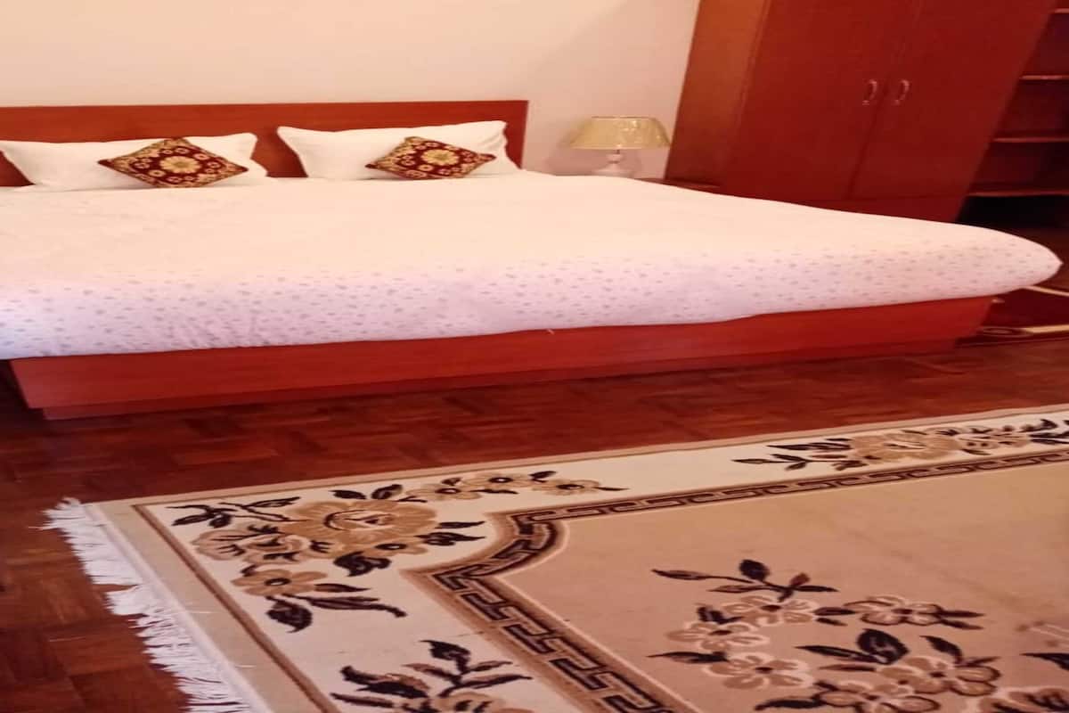 A neatly arranged bedroom with a wooden bed, a floral-patterned rug, and a potted plant.
