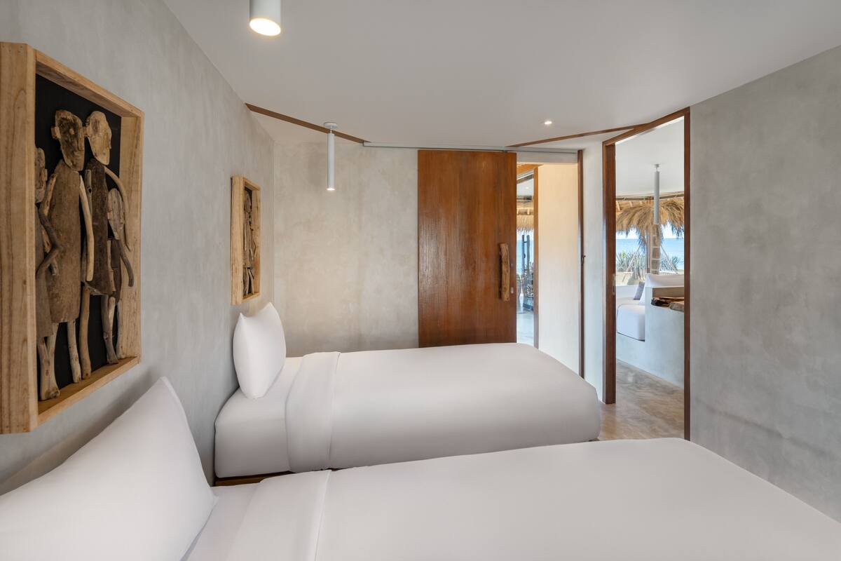 A modern bedroom with two white beds, a wooden headboard, and a large painting on the wall.