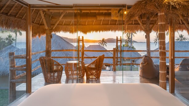 Una stanza con un letto grande, poltrone in vimini e vista sull'oceano al tramonto.
