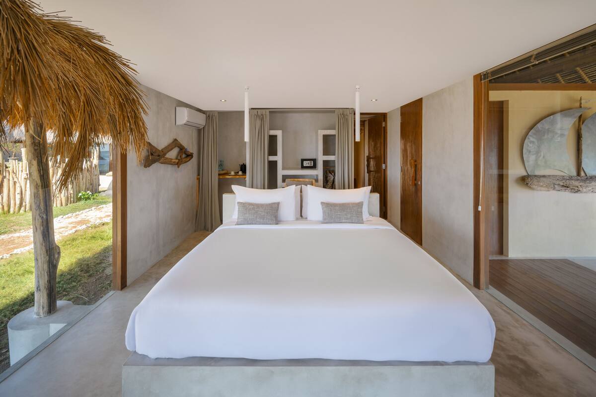 A large bed with white linens, a wooden headboard, and a view of a garden.