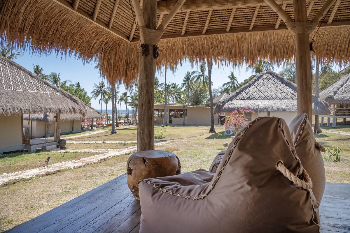 A thatched-roof pavilion with a wooden deck and a cushioned seating area.