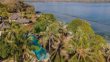 Un resort con piscina circondata da palme, con vista su un ampio specchio d'acqua e montagne.