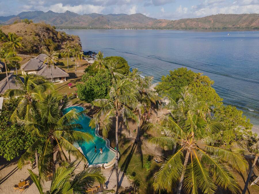 Un resort con piscina circondata da palme, con vista su un ampio specchio d'acqua e montagne.