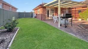 A backyard with a well-maintained lawn, a barbecue grill, and a patio area with chairs.