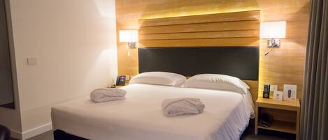 Une chambre d’hôtel avec un grand lit, deux lampes de chevet, une tête de lit en bois et une table de chevet avec un téléphone et un panneau.
