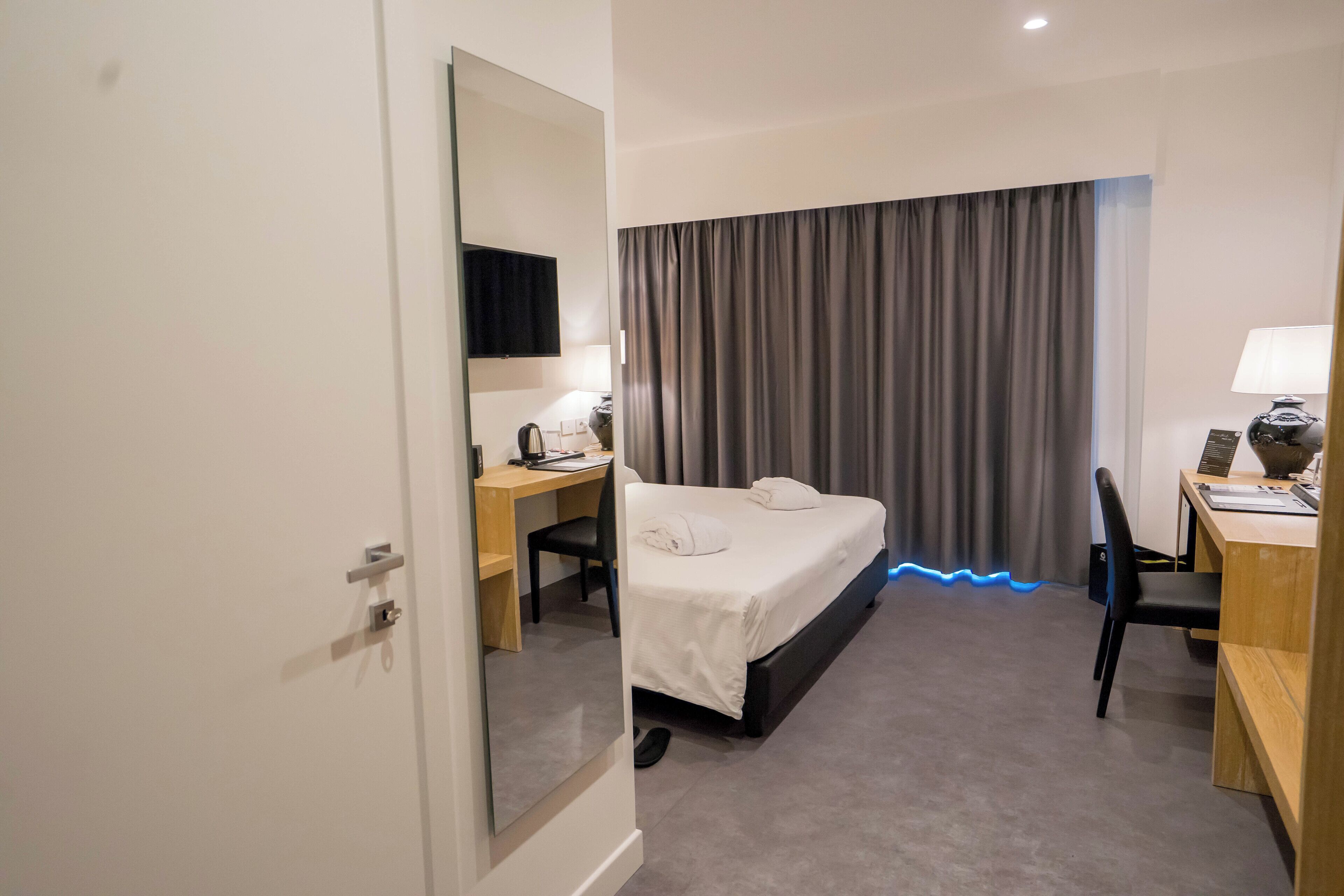 Habitación de hotel con cama, escritorio, silla, lámpara de escritorio y un espejo grande.