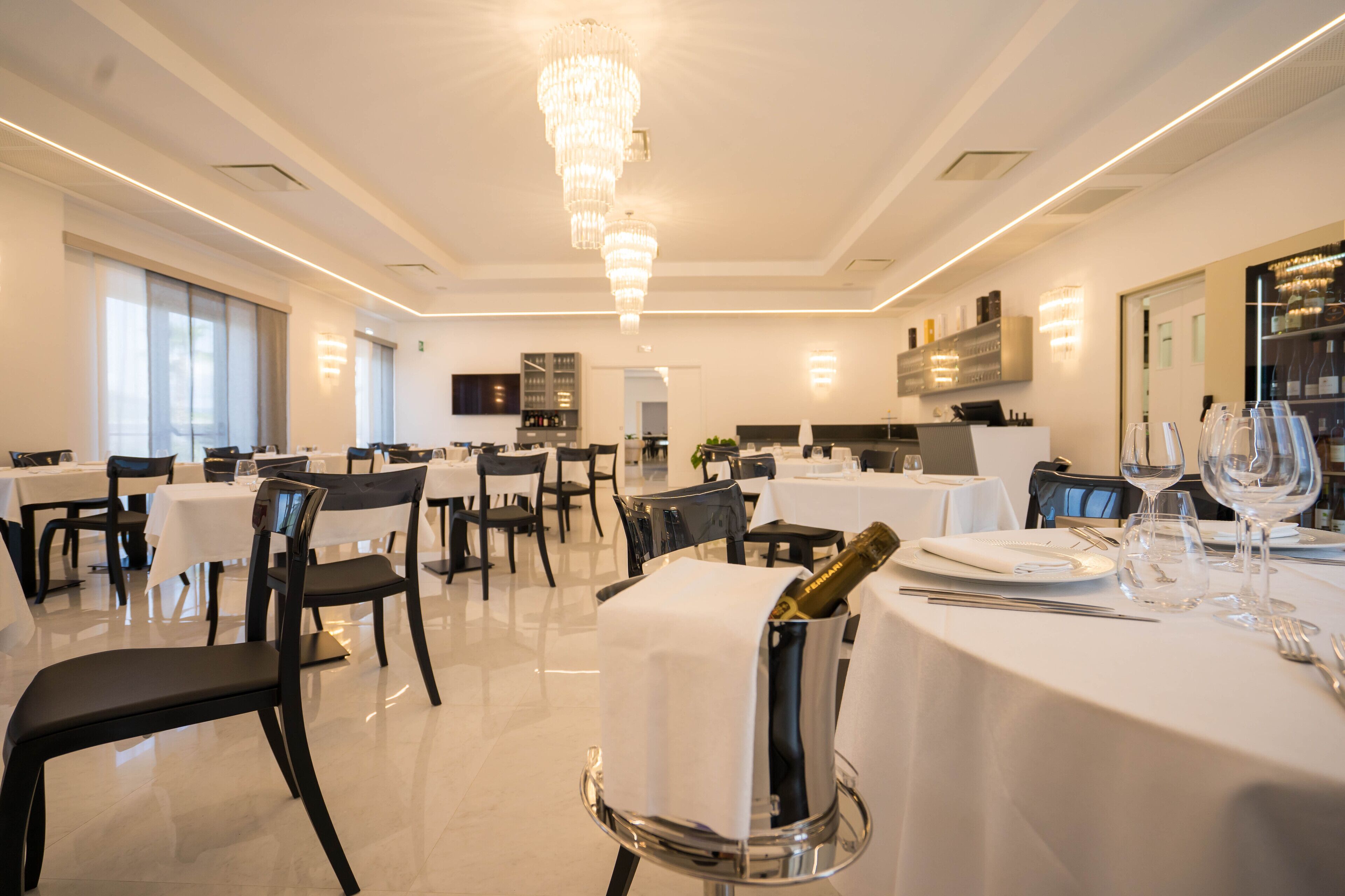 Un espace de restauration moderne avec des tables blanches, des chaises noires et un lustre.