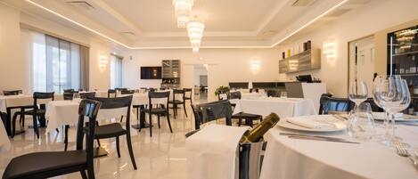 Un espace de restauration moderne avec des tables blanches, des chaises noires et un lustre.