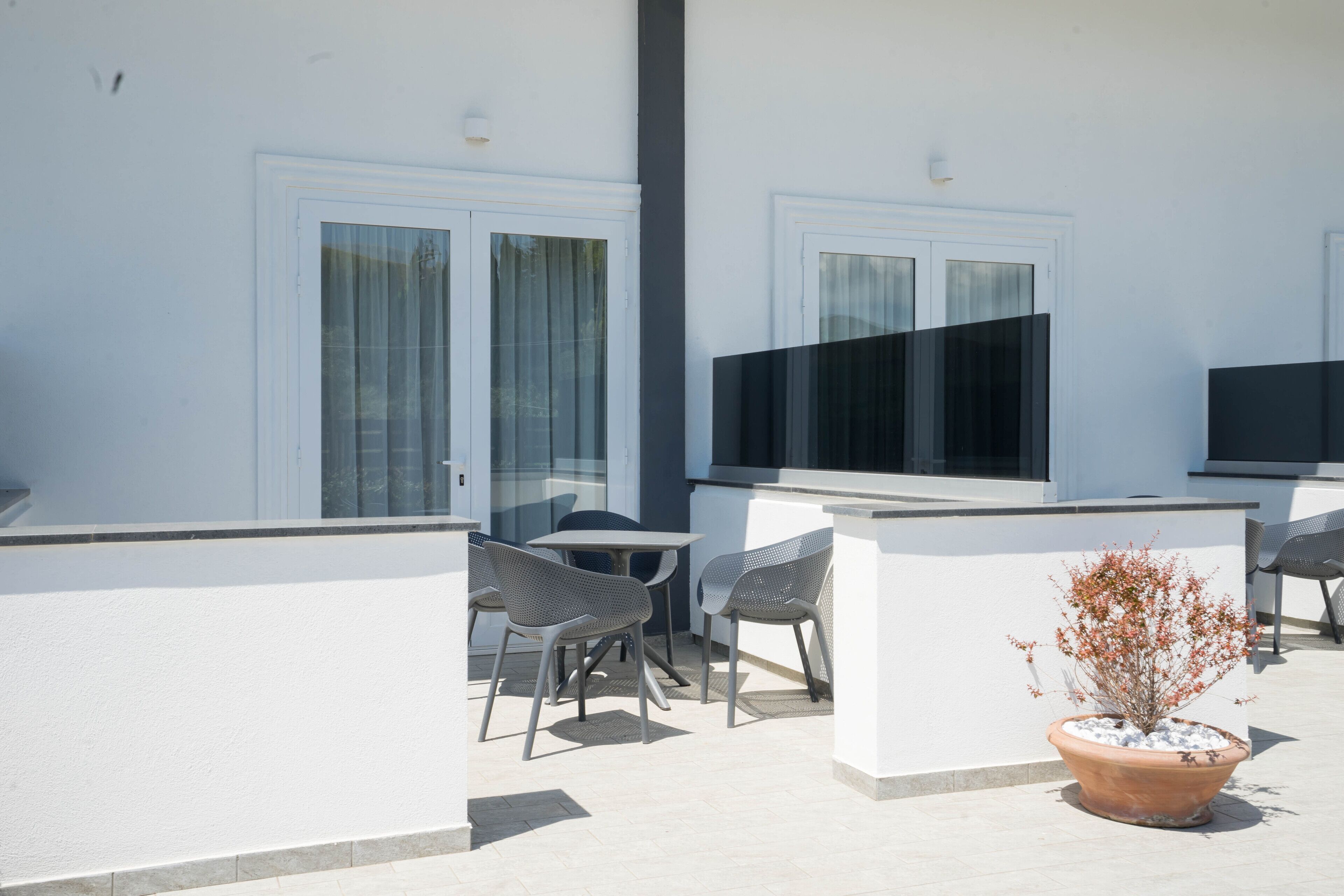 An outdoor patio area with a white wall, two windows, a flat-screen TV mounted on the wall, and a potted plant.