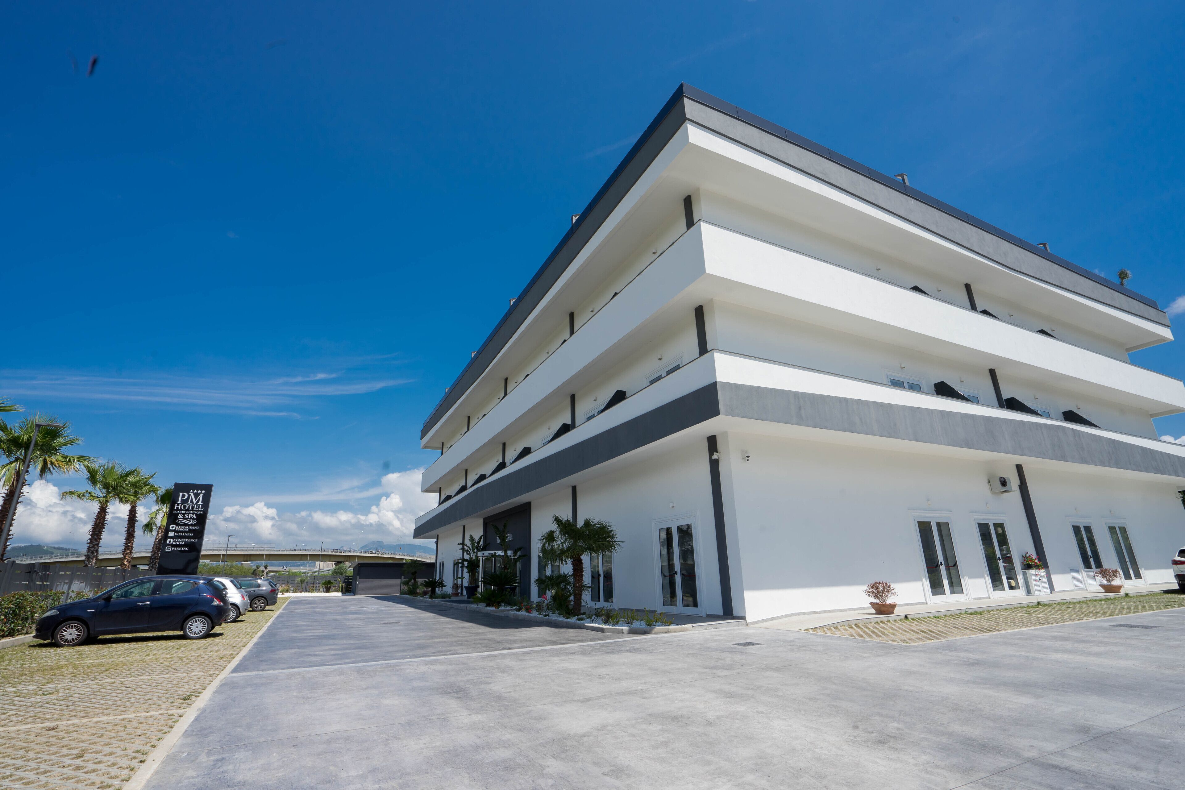 A multi-story hotel with a modern design, featuring a flat roof and a large parking area in front.