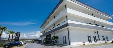 A multi-story hotel with a modern design, featuring a flat roof and a large parking area in front.