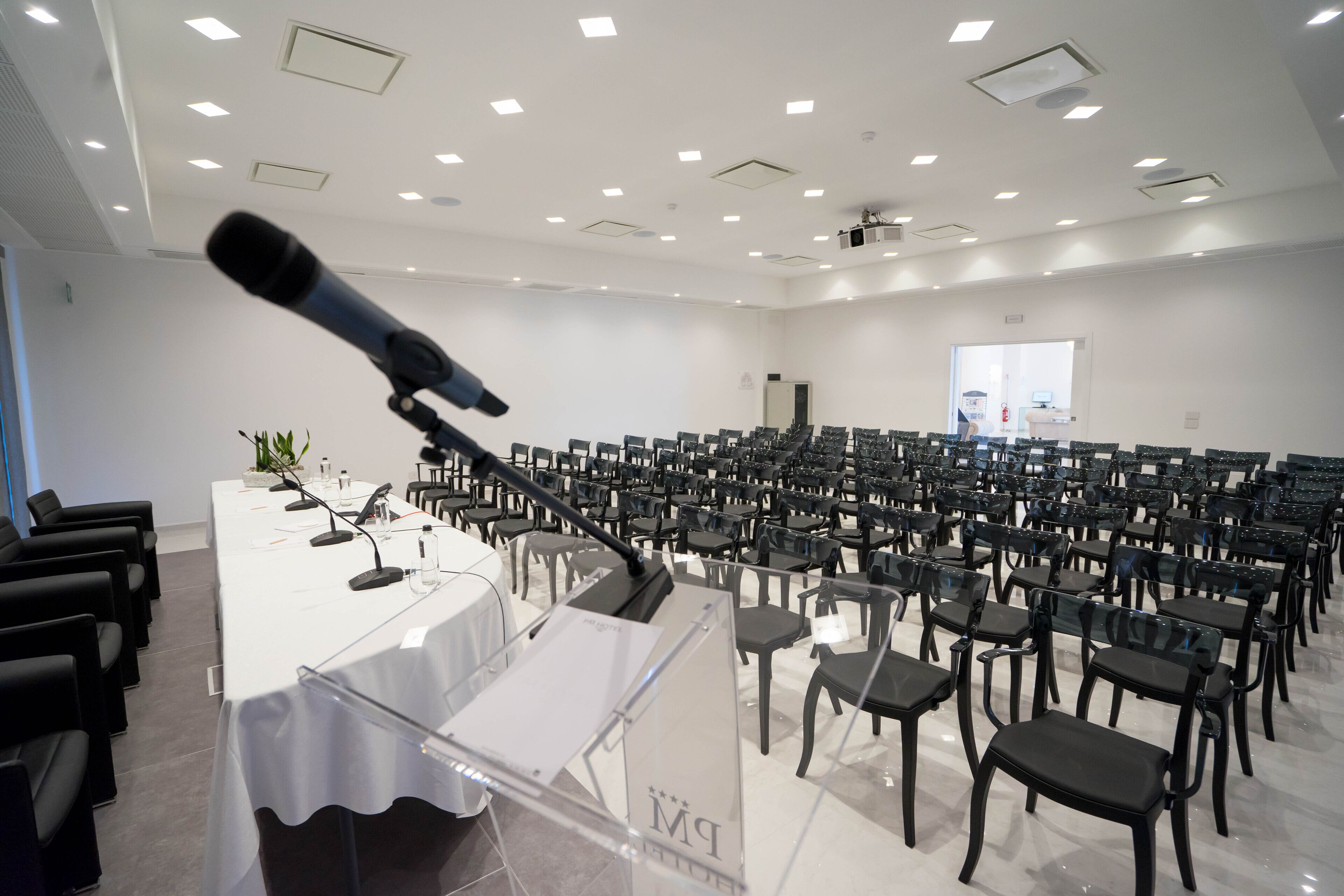 Een vergaderzaal met rijen stoelen, een spreekgestoelte en een microfoon.