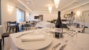 Un comedor con mesas dispuestas para una comida, una botella de vino y copas de vino.