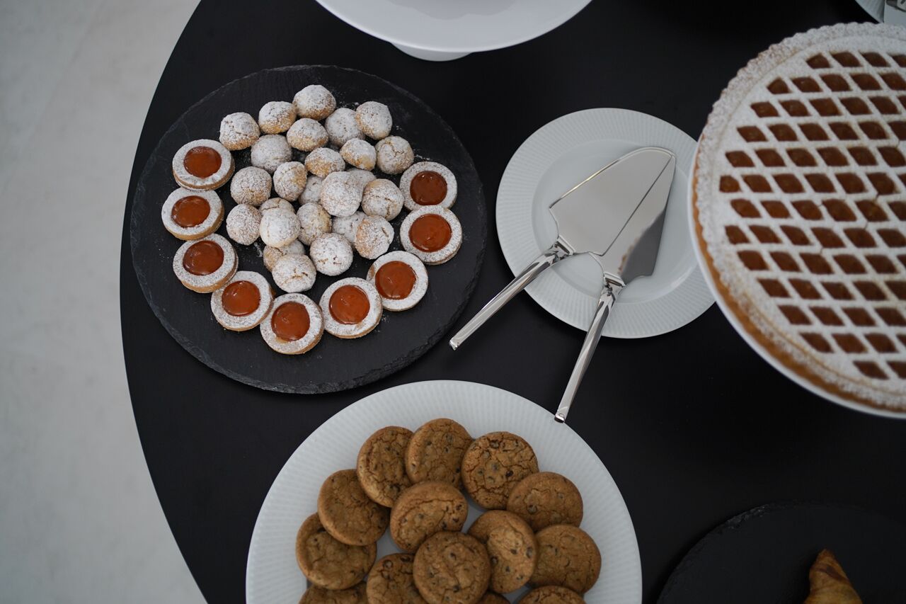 Une table avec des assiettes de biscuits et un gâteau, une spatule à gâteau et une assiette noire en ardoise sur laquelle sont disposés des biscuits.