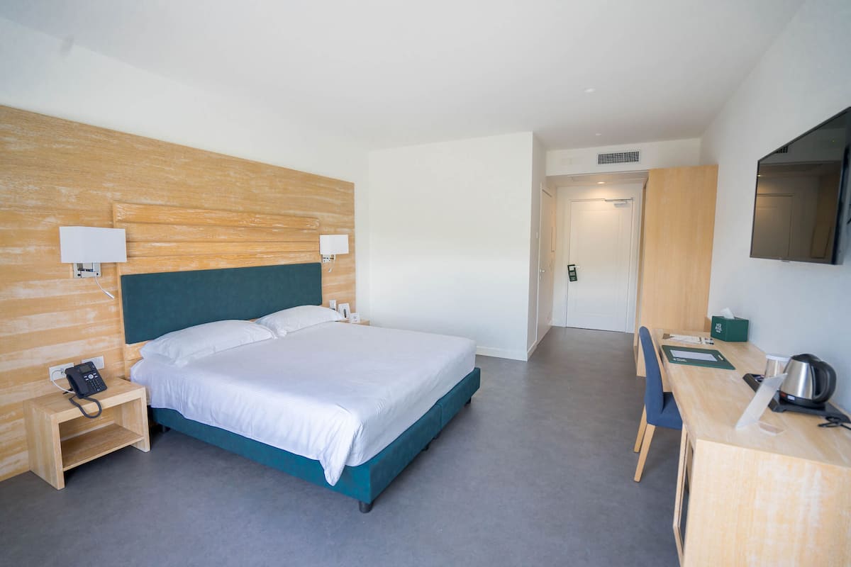 Ein Hotelzimmer mit Bett, Nachttisch, Lampe, Schreibtisch, Stuhl und Fernseher.