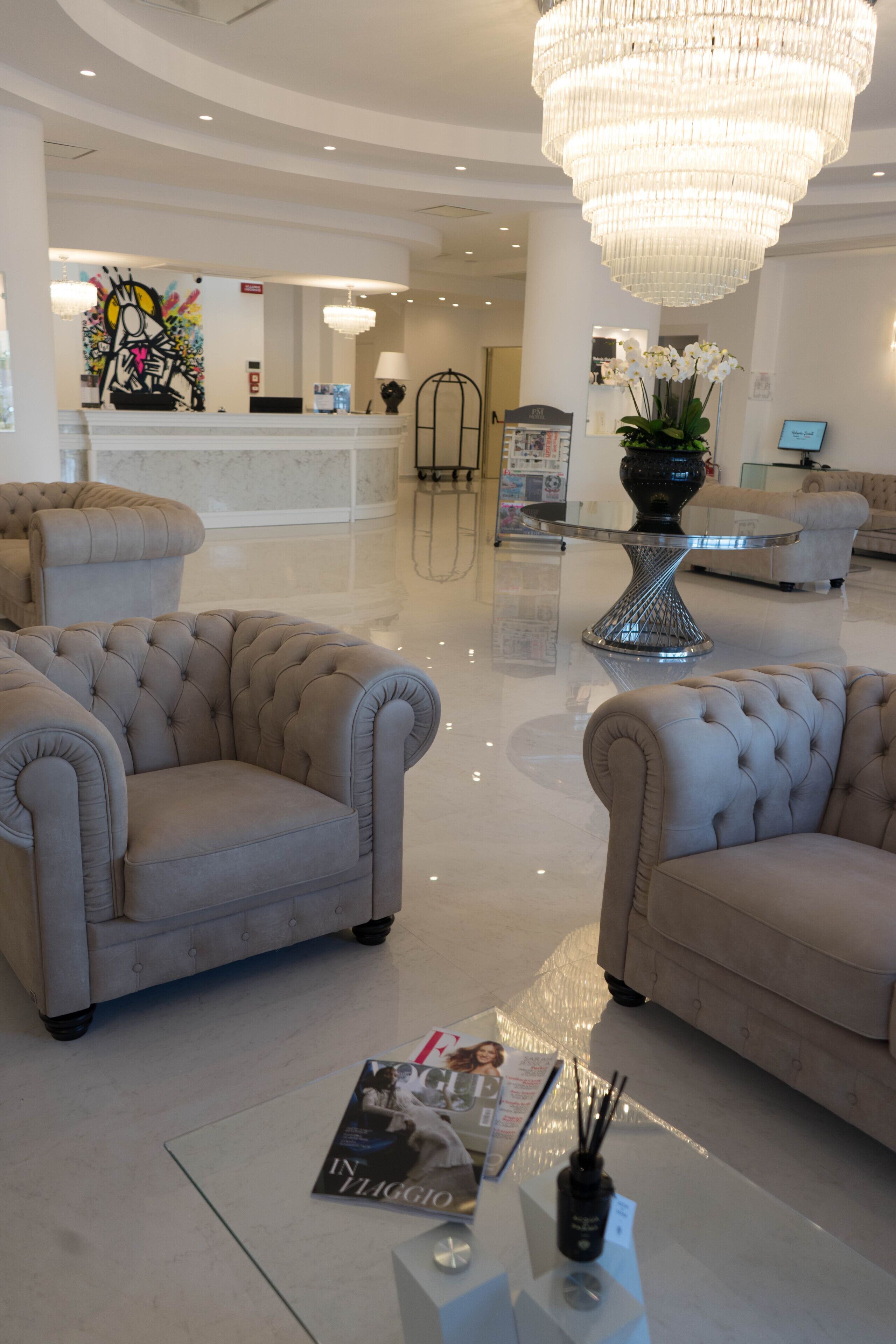 A lobby with two tufted armchairs, a glass coffee table, a chandelier, and a reception desk.