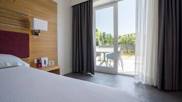 Een hotelkamer met een groot bed, een houten hoofdeinde, een nachtkastje met een afstandsbediening, een brochure en uitzicht op het buitengebied door een schuifdeur.