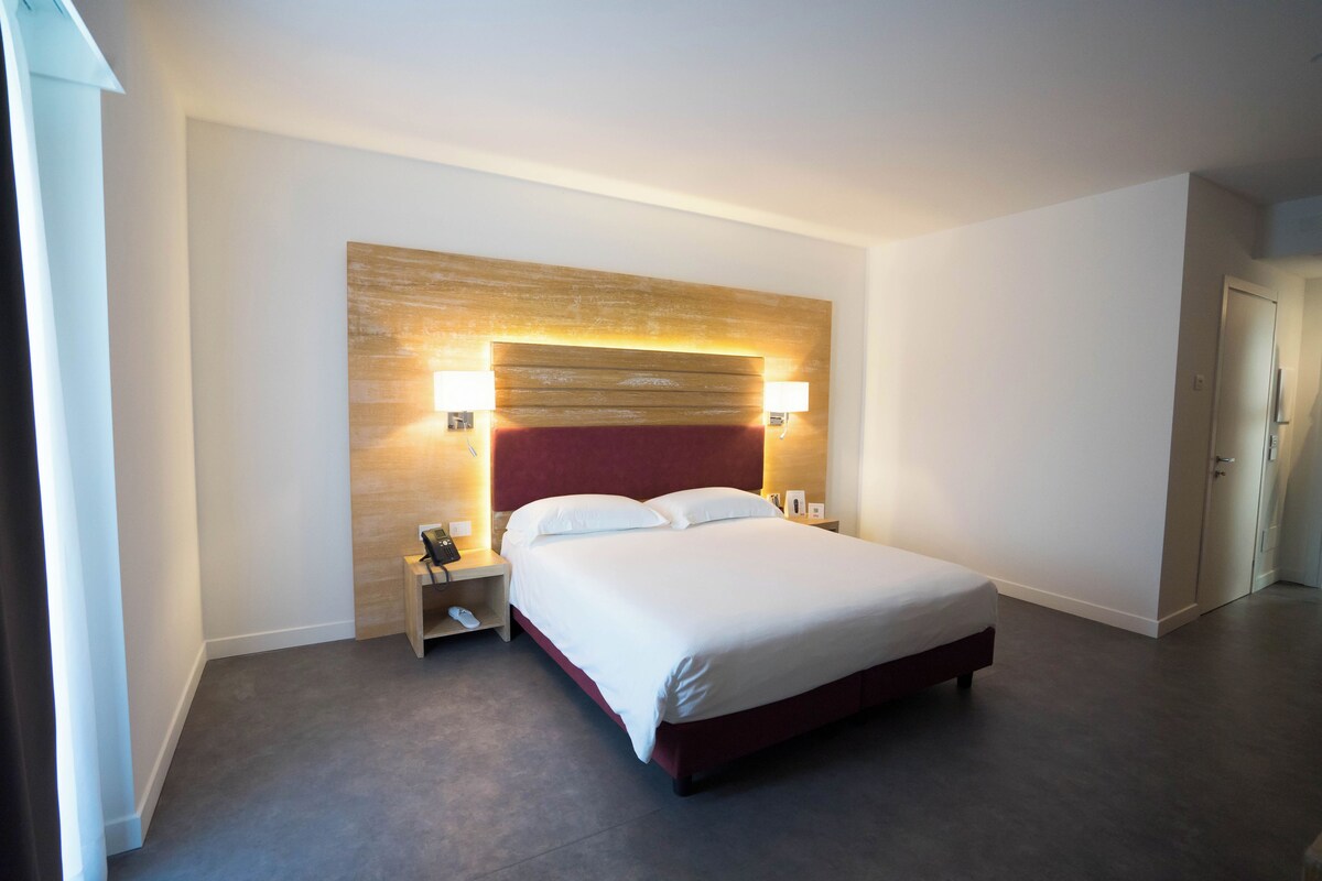 Une chambre d’hôtel moderne avec un grand lit, une tête de lit en bois, des lampes de chevet et une armoire.