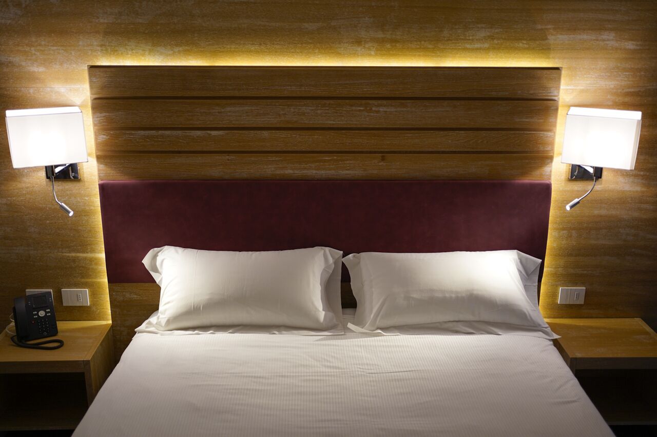 Ein Hotelzimmer mit einem hölzernen Kopfteil, zwei Nachttischlampen, einem Telefon und einem Bett mit weißen Leinen.