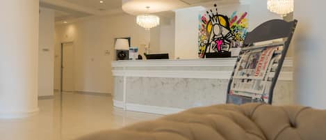 A hotel reception area with a marble counter, a modern chandelier, and a colorful artwork above the counter.