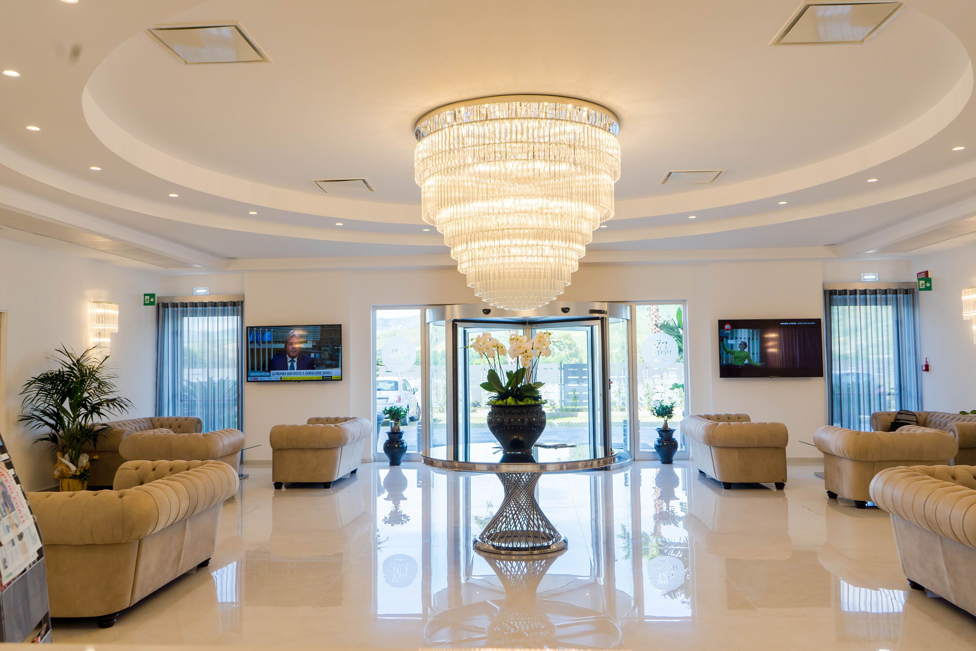 A spacious lobby with a large chandelier, comfortable seating, and a television screen.