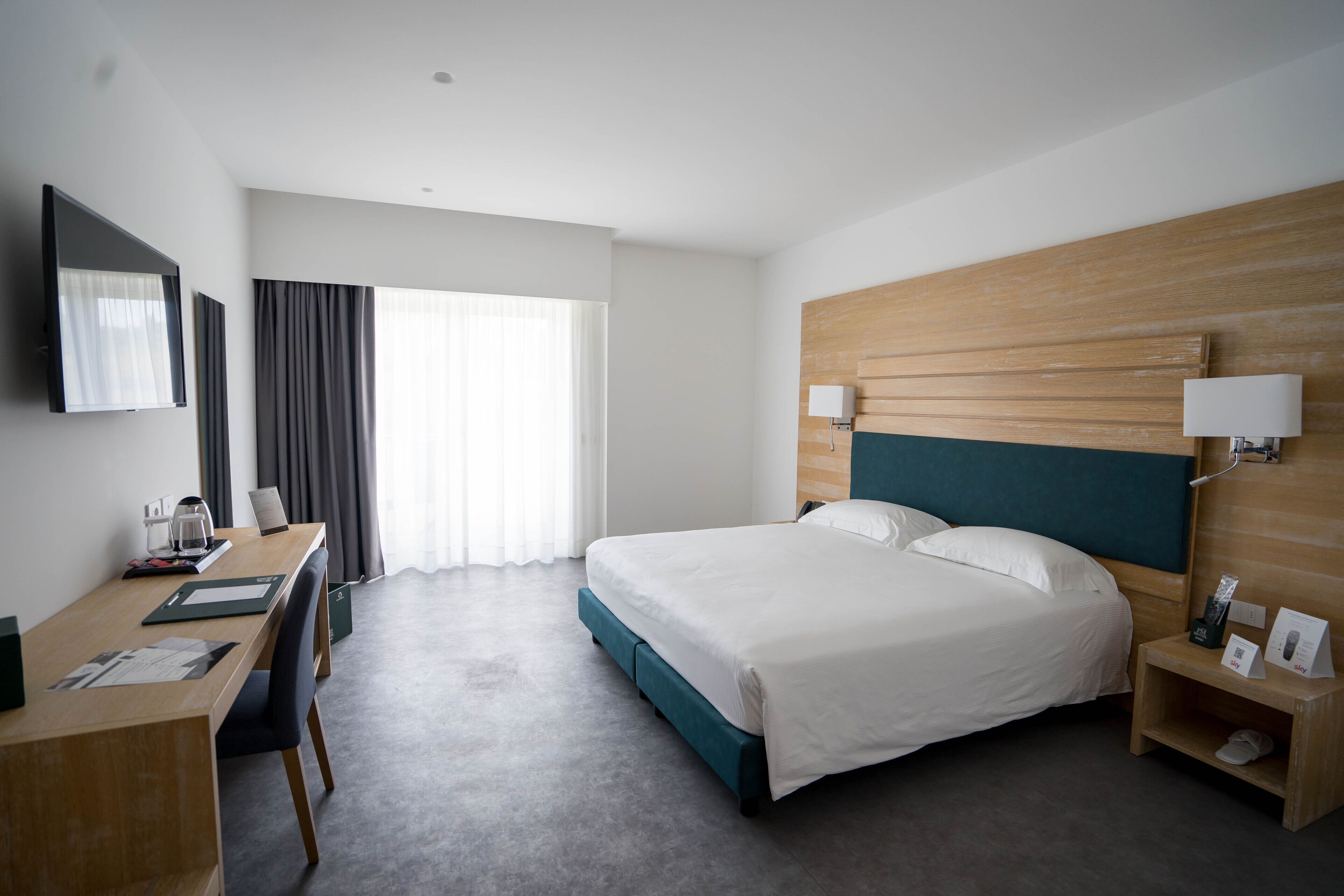 A hotel room with a bed, desk, chair, and a TV on the wall.