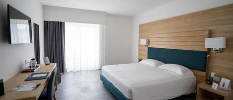 A hotel room with a bed, desk, chair, and a TV on the wall.